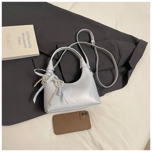 Détail du sac bleu clair avec poignée en perles et ruban sur une veste grise