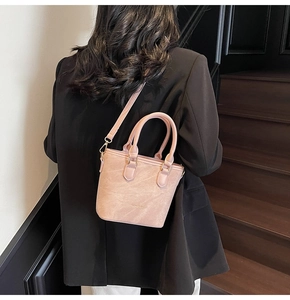 Detail of pink matte bucket bag with gold hardware worn by a model in a black suit