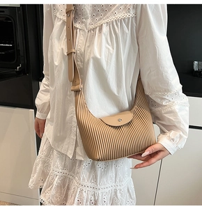 Side view of beige pleated shoulder bag on model with cream dress in a modern home setting