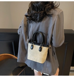 Detail of minimalist beige bucket bag with black leather straps on a grey blazer outfit