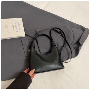 Détail du sac demi-lune noir avec texture cuir et fermeture éclair argentée sur tissu blanc