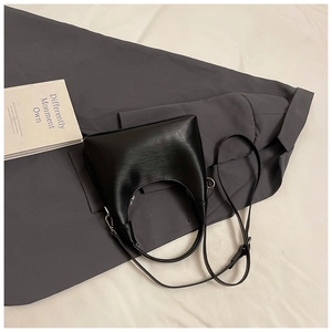 Détails d'un sac hobo en cuir noir avec bandoulière réglable sur un fond au style minimaliste