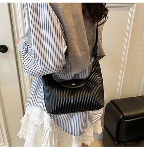 Black pleated shoulder bag with vertical stripe texture worn by a model in casual outfit