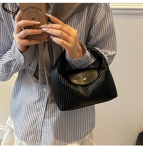 Detail shot of black pleated texture handbag with metal buckle on elegant female outfit