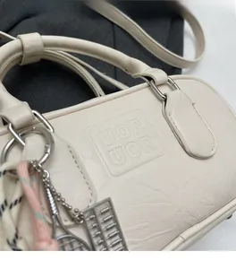 Détail du sac en similicuir crème avec logo embossé et pendentifs décoratifs en métal