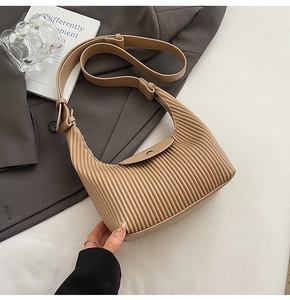 Detail of light khaki pleated shoulder bag with adjustable strap on a grey suit jacket