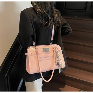 Detailed close-up of pink glossy shoulder bag with golden brand plate and silk scarf