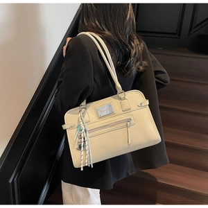 Detail of cream PU leather shoulder bag with bear charm on model in a dark stairwell
