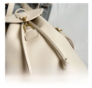 Detail of cream white backpack featuring drawstring closure and bronze metal buckle