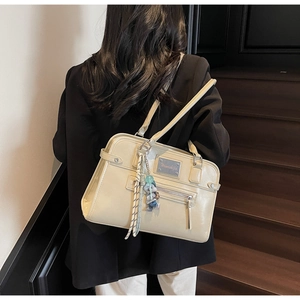 Detail of cream faux leather shoulder bag with silver plaque and cute cartoon charm