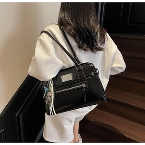 Detail of black glossy shoulder bag showing silver plaque and hanging doll accessory