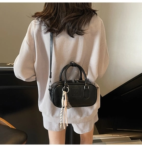 Détail du sac docteur noir avec pendentif tressé et logo embossé porté en bandoulière