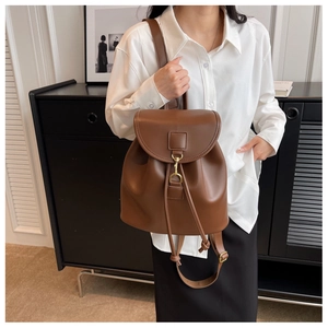 Brown vintage faux leather backpack detail showing front flap and metal buckle on white shirt