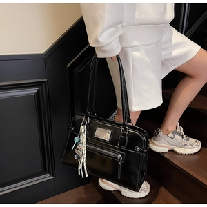 Detail of glossy black vintage tote bag with decorative bear charm on stairs