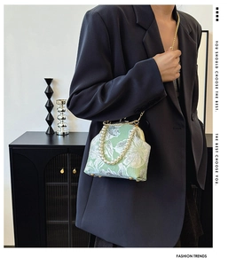 Detail of green floral brocade bag with pearl handle and golden chain on a model