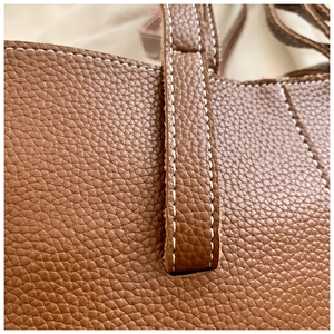 Détail de couture contrastée blanche et grain de litchi sur sac à main en cuir marron
