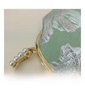 Detail of light green floral jacquard fabric with gold metal frame and pearl handle
