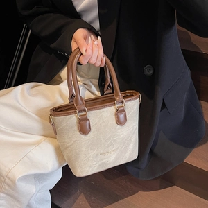 Vintage light gray bucket bag with brown leather trim held by model on wooden stairs