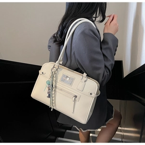 Detail of off-white shoulder bag with front zipper pocket and decorative tassel charm
