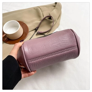 Detail of purple cylindrical leather bag with fine stitching and black metal chain link