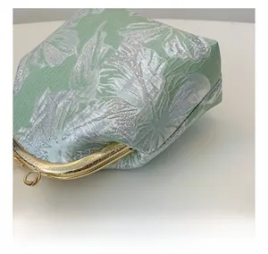 Detail of green and silver leaf jacquard fabric with gold clasp and pearl charm