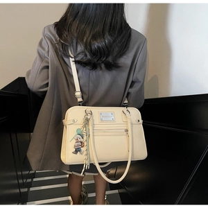 Model view of a large cream shoulder bag with a teddy bear pendant and silver nameplate