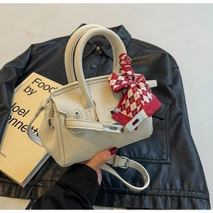 Detail der cremefarbenen Ledertasche mit kariertem Seidenschal-Griff und Drehverschluss