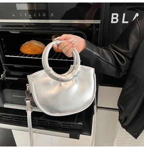Détail d'un sac demi-lune argenté métallisé avec poignée ronde et finition brillante