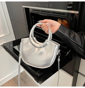 Détail d'un sac à main demi-lune argenté en cuir verni brillant avec anse ronde