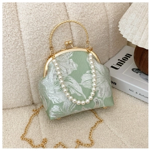 Macro detail of green floral jacquard fabric with gold handle and pearl chain strap