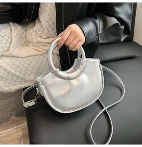 Sac à main argenté en demi-lune porté avec veste en cuir noir et jupe en dentelle