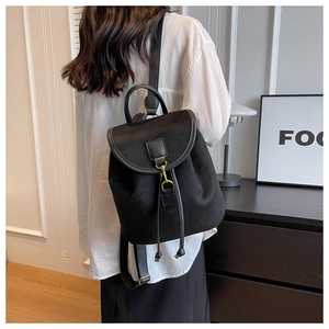 Détail d'un sac à dos en daim noir avec boucle dorée porté par un mannequin en chemise