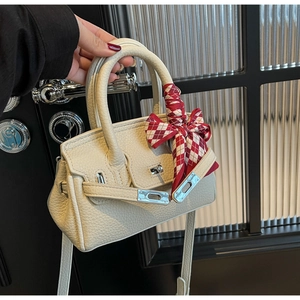Detail der cremefarbenen Lederhandtasche mit Silberschnalle und rot kariertem Seidentuch