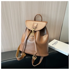Detail of brown textured backpack with flap closure, drawstring, and gold buckles on a sofa