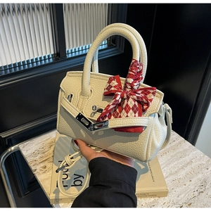 Detail der cremefarbenen Handtasche mit Silberverschluss und rot-weiß kariertem Seidentuch