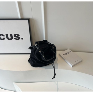 Close-up of black suede bucket bag featuring golden metal eyelets and drawstring closure