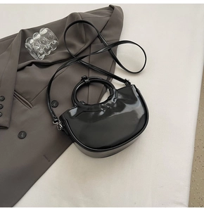Vue détaillée d'un sac à main semi-circulaire en cuir verni noir sur une veste de costume chic