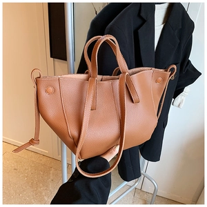 Sac fourre-tout marron à motif litchi porté par un mannequin en tailleur noir