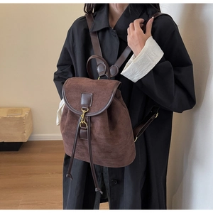 Close-up of a brown suede backpack featuring leather straps and gold metal hardware