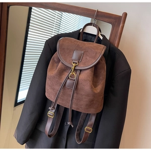 Brown suede backpack with leather trim and gold hook closure styled on a black blazer