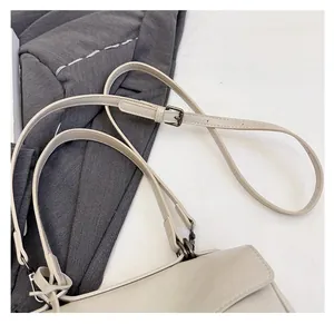 Detail view of the adjustable off-white leather strap with grey metal buckle and stitching
