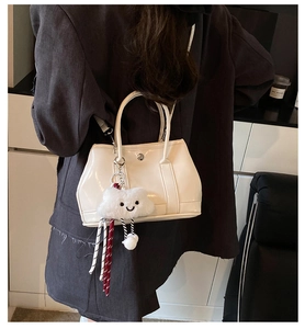 Side view of a glossy cream bucket bag with a cute plush cloud charm on a model
