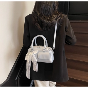 Detail of light beige crossbody bag with lace bow and pearl charm on a black blazer