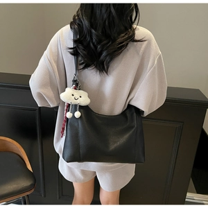 Detail of black crescent tote bag with white plush cloud charm and pebble grain texture