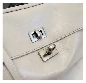 Detail of silver twist-lock hardware on a light beige textured leather shoulder bag