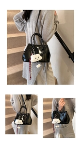 Detail of glossy black handbag with fluffy white cloud charm and striped woven pendant