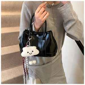 Close-up of black glossy patent leather bucket bag with cute white cloud plush charm detail