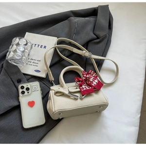 Detail der cremefarbenen Mini-Handtasche mit Kiesellederstruktur und rot kariertem Seidenschal