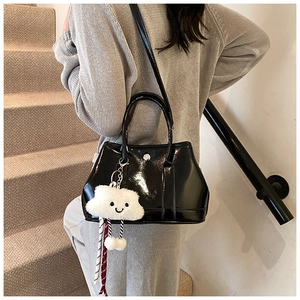 Detail of a black patent leather bucket bag with a white plush cloud charm on a model