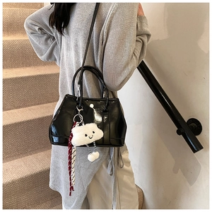 Glossy black bucket bag with plush cloud charm shown in a casual lifestyle setting